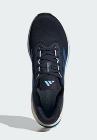 Zapatilla de running de malla en color navy con acentos en azul claro, suela acolchada y un patrón texturizado en la parte superior. Etiquetada como "SUPERNOVA".