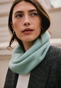 Cowl neck scarf in mint green ribbed knit, soft texture, layered design, worn over a white top and dark textured blazer.