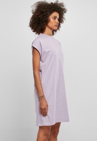 Robe en coton lavande clair avec des manches roulées courtes, coupe ample et longueur genou. Texture lisse, détails minimaux.