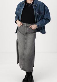 Jeansjacke, blau; schwarzes, figurbetontes Oberteil; hochgeschnittenen, graue Jeans-Maxi-Rock mit seitlichen Schlitzen; schwarze Sneaker. Einfaches Design, klassischer Stil.
