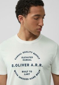 Witte katoenen t-shirt met zwarte ronde tekst: "CASUAL QUALITY SUPPLY", "S.OLIVER A.R.R.", en "BUILT TO LAST". Ronde halsontwerp.