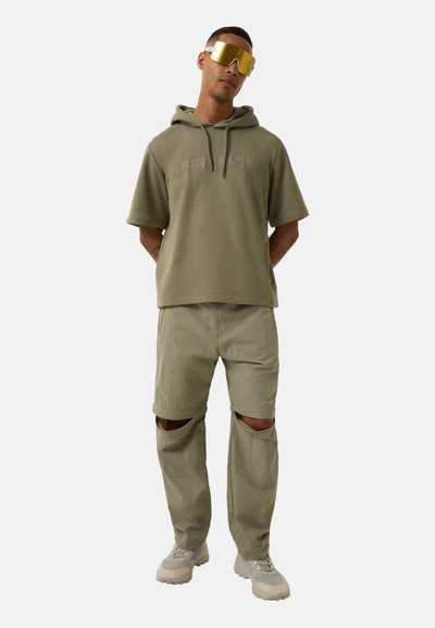 Hellgrüner, übergroßer Hoodie mit dem Schriftzug "FIRE", kombiniert mit hellgrünen Cargo-Hosen mit Knieausschnitten und beigen Sneakern.