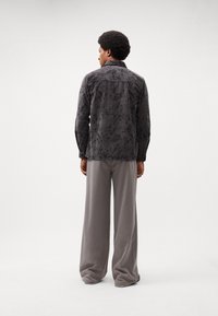 Chemise noire à manches longues avec un motif floral, associée à un pantalon large gris. La chemise possède un col et des poignets boutonnés.