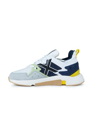 Zapatilla deportiva blanca con acentos en azul marino y verde claro, materiales de ante y malla, punta redondeada, suela acolchada y una suela de goma texturizada.