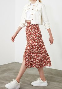 Veste en denim blanche sur un crop top, associée à une jupe florale marron avec une fente sur le côté. Portée avec des baskets blanches.