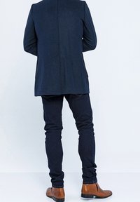 Marinblå skräddarsydd kavaj med en ren silhuett, tillsammans med mörk denim slim-fit byxor och bruna läderankelstövlar. Släta texturer, minimal detaljering.