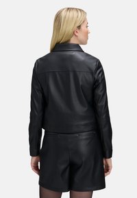 Zwarte leren jas met een cropped ontwerp, een notch-kraag en een gladde textuur. Heeft minimale stiksels en een schone, gestroomlijnde silhouet.