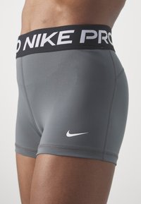 Gros plan d'une personne portant un short de sport Nike Pro gris avec une ceinture noire et le logo swoosh blanc sur la cuisse.