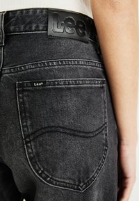 Zwarte denim jeans met een leren label op de tailleband dat "Lee" in reliëf heeft. De achterzakken hebben subtiele stikdetails.