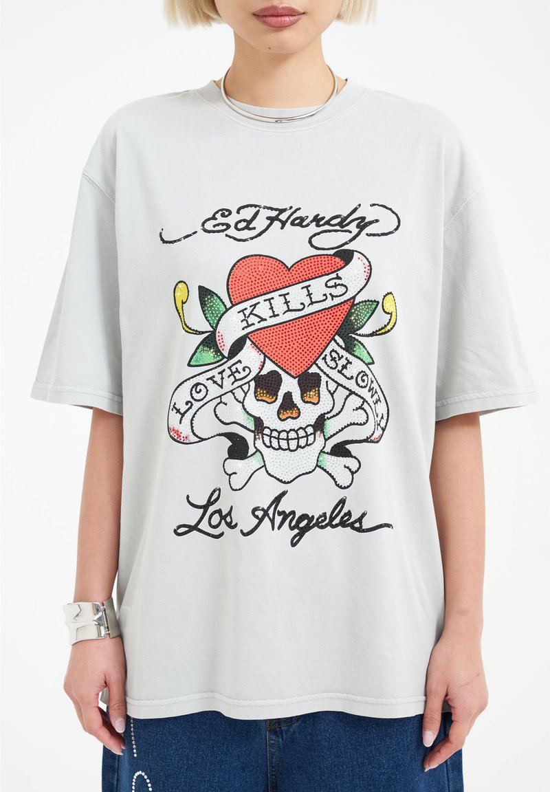 Gray oversized t-shirt featuring a colorful print of a heart, skull, and text, with a soft cotton texture and short sleeves.