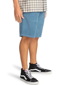 Pantaloni corti in corduroy blu con tessuto texturizzato, tasche laterali e lunghezza sopra il ginocchio, abbinati a sneakers alte nere.