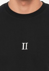 Camiseta de algodón negra con cuello redondo, que presenta un gráfico blanco "II" centrado en el pecho. Textura suave y diseño ajustado.
