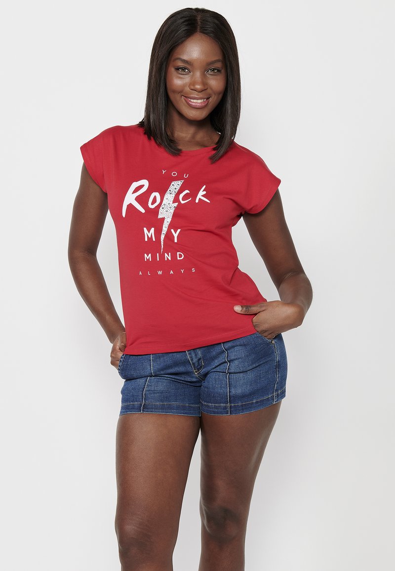 Camiseta roja de manga corta con gráficos en blanco, que presenta un diseño de rayo y el texto "Siempre me vuelas la cabeza". Se lleva con pantalones cortos de denim.
