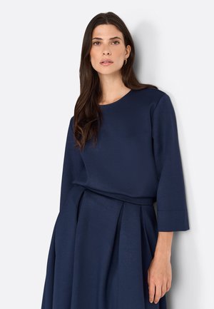 Abito blu navy con scollatura tonda, maniche lunghe e corpetto aderente. Presenta una gonna plissettata, realizzata in un tessuto liscio e strutturato.