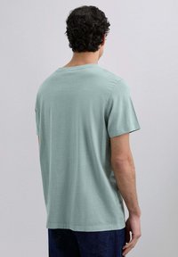 Lichtgroene t-shirt met korte mouwen van zachte stof, voorzien van een ronde halslijn en een ontspannen pasvorm. Achteraan is de gladde textuur en het eenvoudige ontwerp te zien.