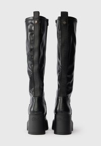 Μαύρες μπότες μέχρι το γόνατο από λείο δέρμα, με πίσω φερμουάρ και ανάγλυφα λογότυπα στα πλάγια. Χοντροί μπλοκ τακούνια.