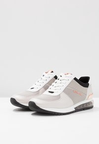 Jasnoszare buty sportowe wykonane są z siateczki i syntetycznej skóry, mają okrągły czubek, czarne akcenty oraz przezroczystą podeszwę z poduszką powietrzną.