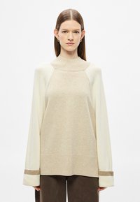 Μπεζ και εκρού πλ�εκτό πουλόβερ με ψηλό γιακά, φαρδιά εφαρμογή, ριμπ μανσέτες και υφή με ανάγλυφο φινίρισμα. Μαλακό ύφασμα με αντιθετικές λεπτομέρειες.