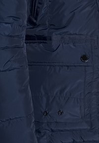 Giacca puffer blu navy con texture trapuntata, dotata di una tasca frontale con chiusura a scatto nera e dettagli di cucitura rinforzata.