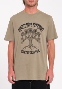 Oliven grøn bomulds t-shirt med et sort grafisk design af et slange-træ og teksten "VOLCOM STONE EARTH TRIPPER." Korte ærmer, afslappet pasform.