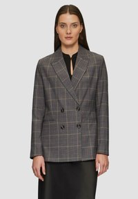 Grijze geruite dubbelknopen blazer met twee voorzakken, zwarte knopen en ingevouwde revers. Gestyled over een zwarte blouse.