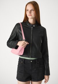Giacca in pelle nera con colletto rialzato, zip e dettagli trapuntati sulle spalle. Abbinata a pantaloni corti neri e una borsa testurizzata rosa.