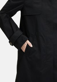 Schwarze, leichte Jacke mit glatter Textur, ausgestattet mit einer Brusttasche, seitlichen Taschen und knöpfbaren Manschetten. Minimalistische Designdetails sind enthalten.