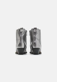 Botas de tobillo plateadas metálicas con textura suave, diseño estructurado, tacón apilado y cierre de cremallera, con costuras decorativas.