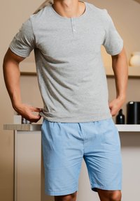 Camisa de algodón gris de manga corta con cuello de tres botones, combinada con pantalones cortos a rayas azules. Textura suave y corte relajado.