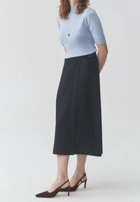 Jasnoniebieski dopasowany top z krótkimi rękawami, zestawiony z czarną spódnicą do kolan z boczną zakładką oraz smukłym brązowym butem na wysokim obcasie.