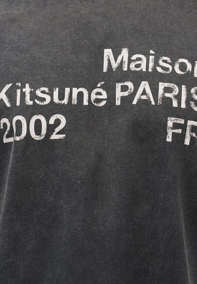 Σκούρο γκρι ύφασμα με φθαρμένο λευκό κείμενο που γράφει "Maison Kitsuné PARIS 2002 FR".