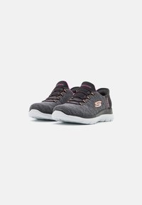 Ein Paar graue und schwarze Skechers Sportschuhe mit pinken Akzenten und weißen Sohlen auf einem schlichten weißen Hintergrund.