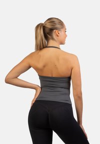 Grijze sporttop met een aansluitend ontwerp en dunne bandjes, gecombineerd met strakke zwarte leggings. Glad materiaal met een lichte glans.