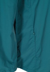 Teal jakke med en glat tekstur, en afslappet pasform, sidelæg og en lille lynlåsdetalje. Minimalistisk design uden synligt hardware.