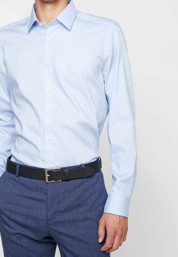 Lichtblauw button-up shirt met een puntige kraag, met een subtiele textuur. Gecombineerd met donkerblauwe broek en een zwarte riem.