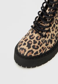 Ankelstøvle med leopardmønster, der har en tekstureret overflade, sorte snørebånd og en kraftig sort gummisål.