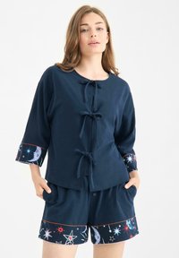 Granatowa bluzka z krótkim rękawem z kokardkami, z wzorzystymi mankietami. Połączona z granatowymi szortami ozdobionymi wzorami gwiazd i księżyca.
