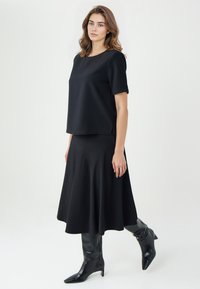 Czarny top z krótkim rękawem połączony z czarną spódnicą w kształcie litery A. Strój ma gładką fakturę i luźny krój. Dobrany z wysokimi botkami.