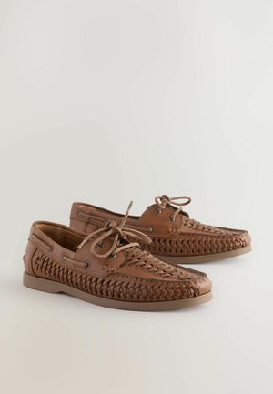 Brown leather boat shoes with woven texture, round laces, and metal eyelets. Flat sole and a casual design suitable for various occasions.