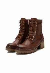 Botas de tobillo de cuero marrón con un diseño de cordones, cremallera lateral, accesorios en tono dorado, acentos texturizados y un tacón grueso.