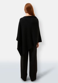 Czarny ponczo wykonane z miękkiego, teksturowanego materiału, o luźnej, zwiewnej sylwetce bez zapięć, noszone na czarnych szerokich spodniach.