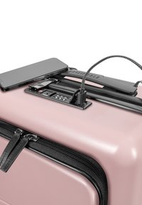 Różowa walizka twarda z czarnymi akcentami, podwójne zamki błyskawiczne, wbudowany port do ładowania i kabel USB. Na górze znajduje się smartfon.