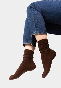 Brązowe, prążkowane skarpetki wykonane z miękkiego materiału, z marszczonym ściągaczem i dopasowanym krojem, zestawione z krótkimi niebieskimi dżinsami.