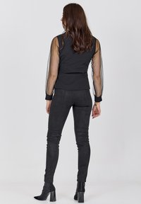 Sort top med gennemsigtige puffærmer, parret med sorte faux suede tætsiddende bukser og stiletter. Enkel, slank design uden mønstre.