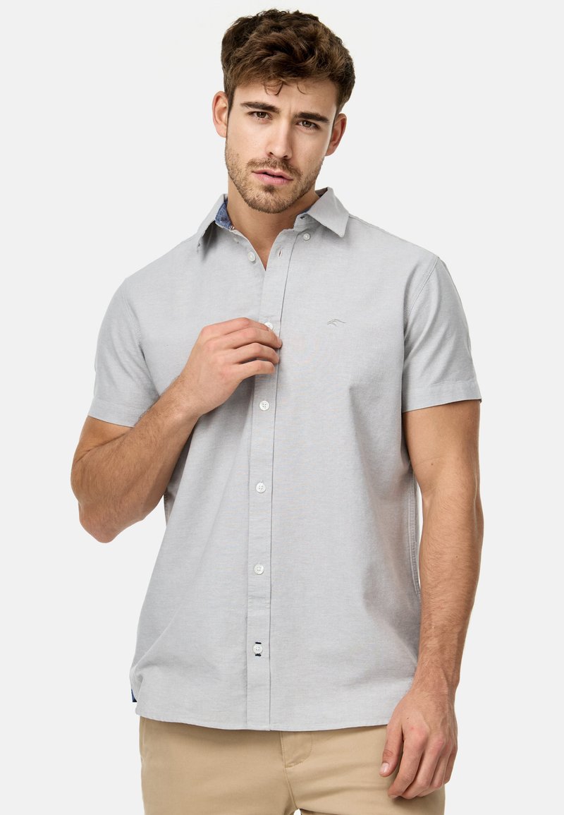 Camisa de botón de manga corta color gris claro con cuello, que presenta un patrón sutil y un logotipo bordado en el lado izquierdo del pecho.
