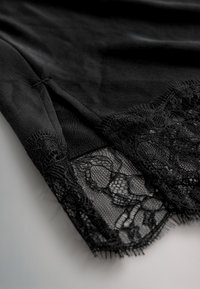 Schwarzer Stoff mit floralen Spitzendetails und transparentem Mesh-Einsatz, der die Textur und das filigrane Muster am Saum des Kleidungsstücks zeigt.