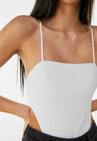 Vitt ribbat bodysuit med tunna axelremmar och sidokut, med fyrkantig halsringning och textilierad yta, i kombination med mörka denimjeans.