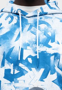 Μπλε γραφική φούτερ με λευκές λεπτομέρειες, με σχέδιο πιτσιλιάς από γράμματα και σχήματα, κορδόνια και μαλακή υφή.