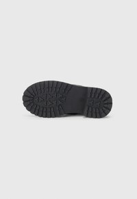 Semelle en caoutchouc noir avec un motif de texture et des crampons proéminents pour une meilleure traction, conçue pour la stabilité et l'adhérence.