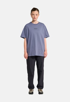 Lilla oversized t-shirt med "HALO" i sort tekst, parret med sorte løstsiddende bukser og beige sneakers. Glat bomuldsstof, afslappet pasform.